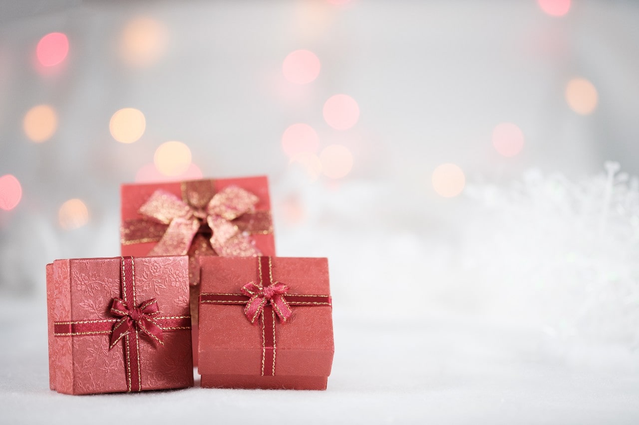 Three red jewelry gift boxes nest together in front of a white Christmas tree
