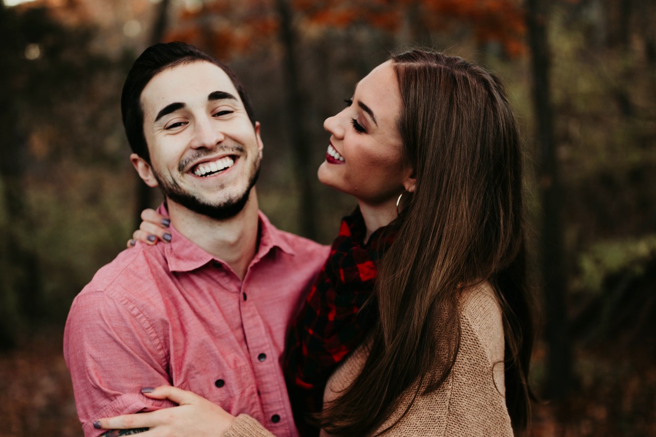 A couple smiling and holding each other on a walk through the woods