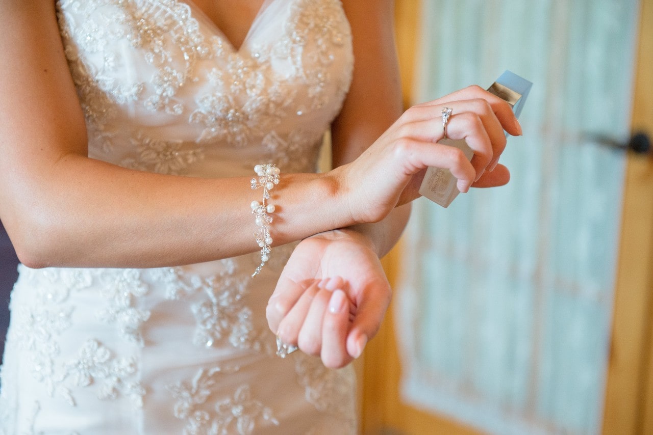 A spring bride putting perfume on her wrists and showing her floral-motif pearl bracelet that matches the flower embellishments on her wedding dress