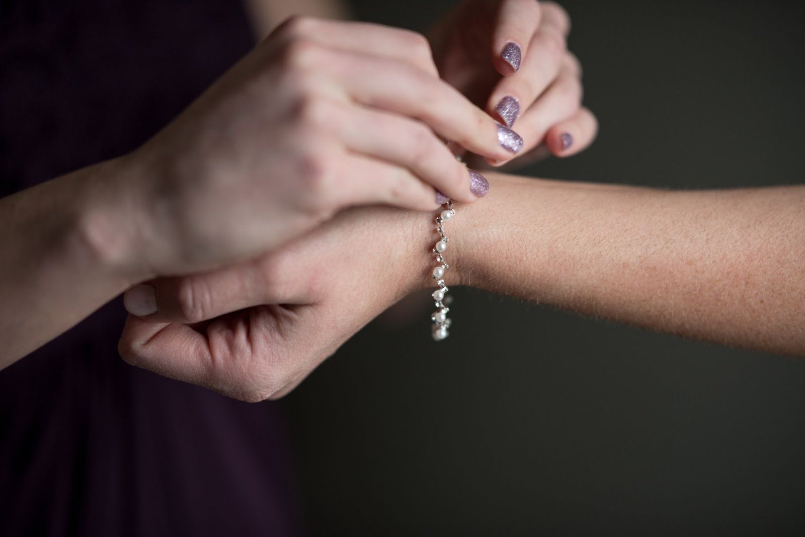 A bridesmaid putting a platinum and pearl bracelet on a bride