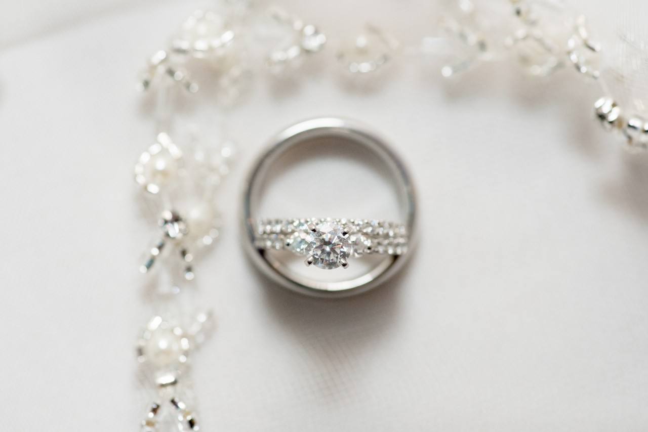 A diamond and platinum engagement ring with a platinum wedding band and a pearl necklace around it