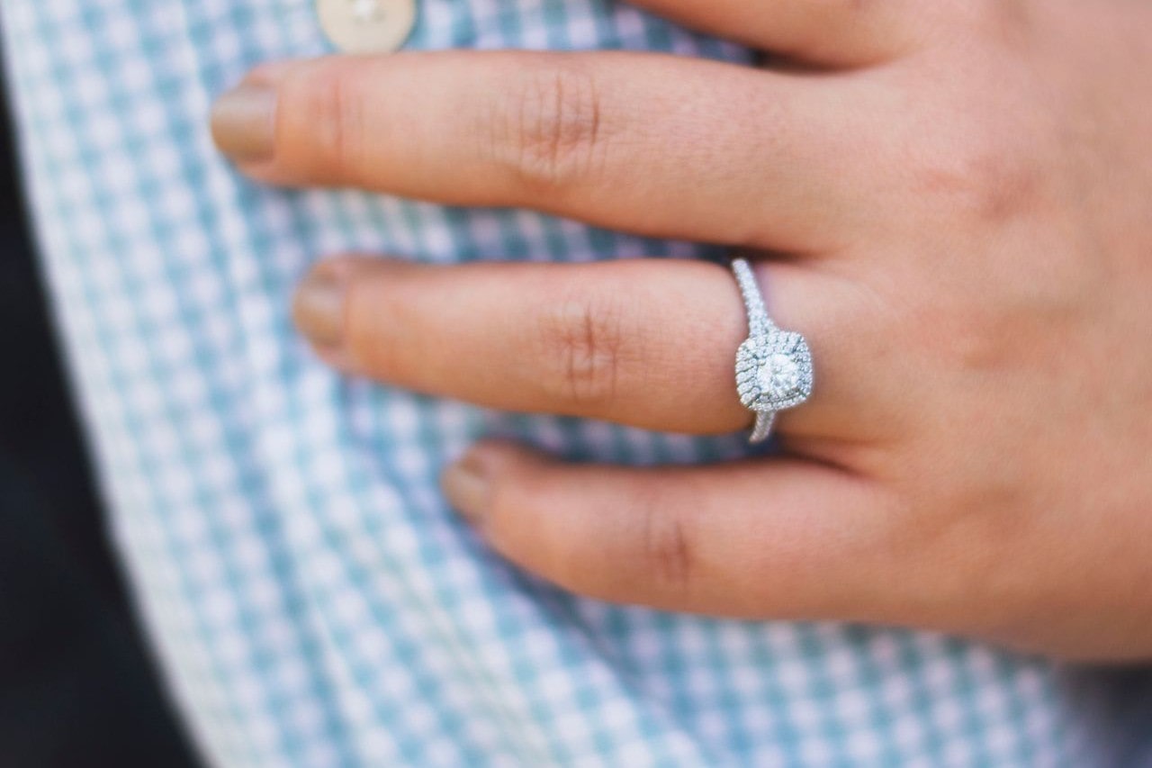A woman wearing a halo diamond engagement ring touches her fiance’s arm