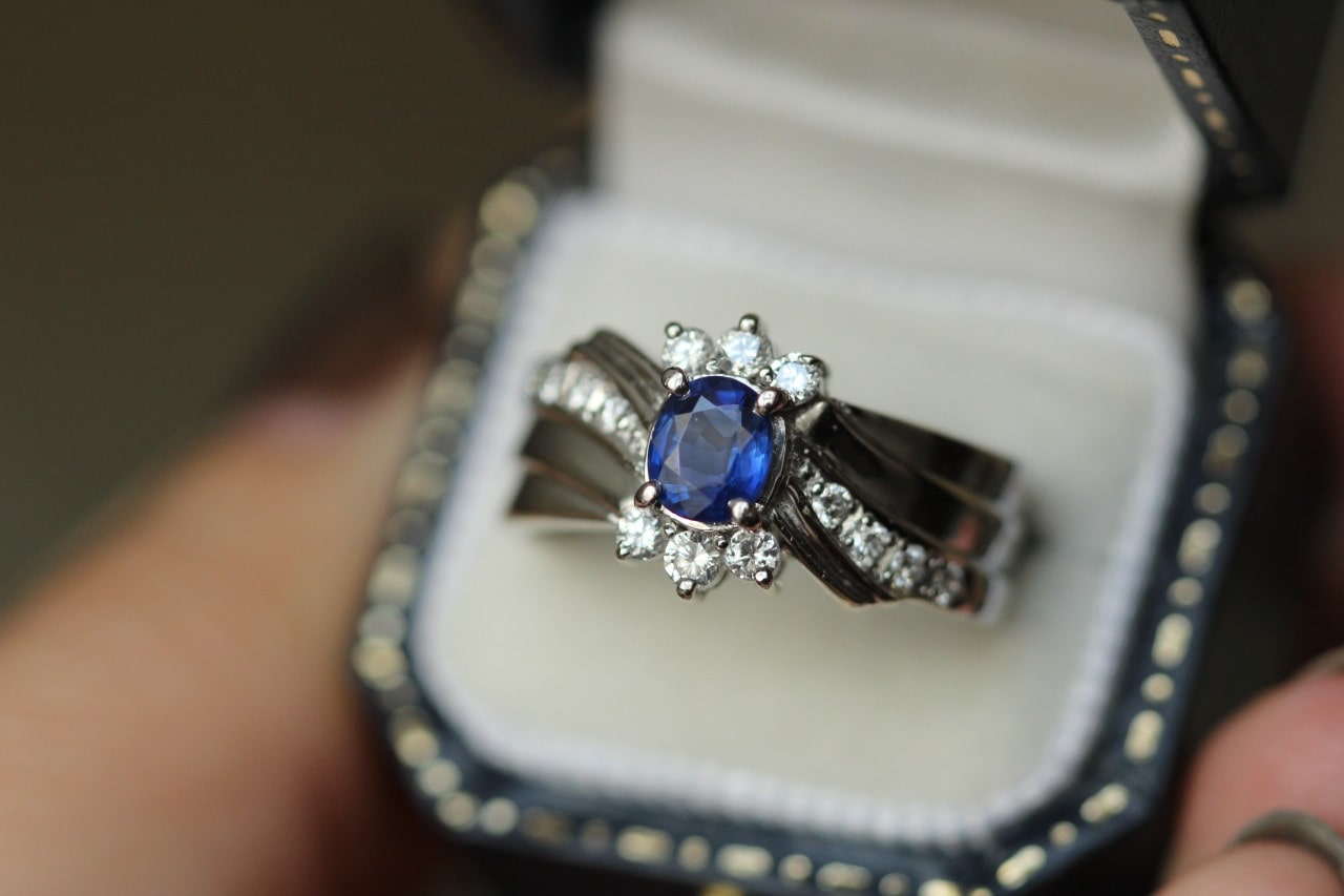 A man inspects an engagement ring with a sapphire center stone before popping the question to his beloved