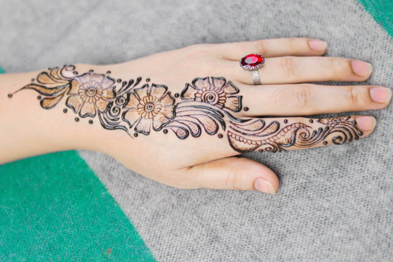 A woman sporting a sterling silver ruby engagement ring rests her hand on a cotton picnic blanket while she waits for her henna to dry