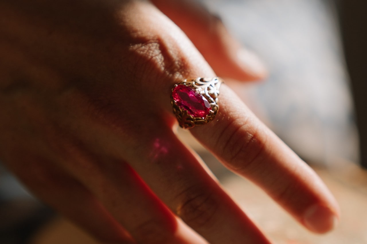 A woman wearing a gold engagement ring with a pink topaz center stone sits on her index finger