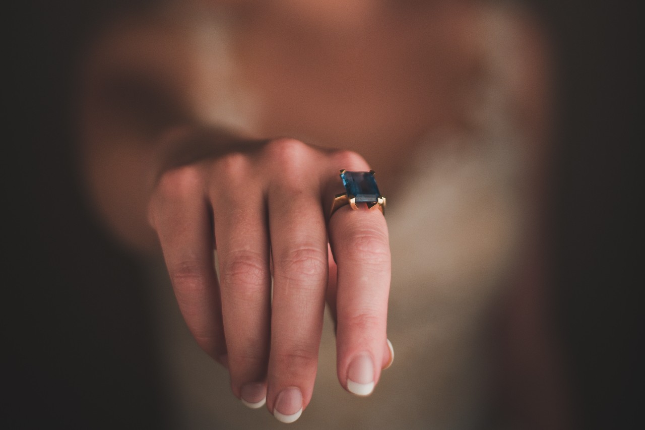 A woman wearing an emerald-cut emerald engagement ring on her index finger as she reaches out for her lover’s hand