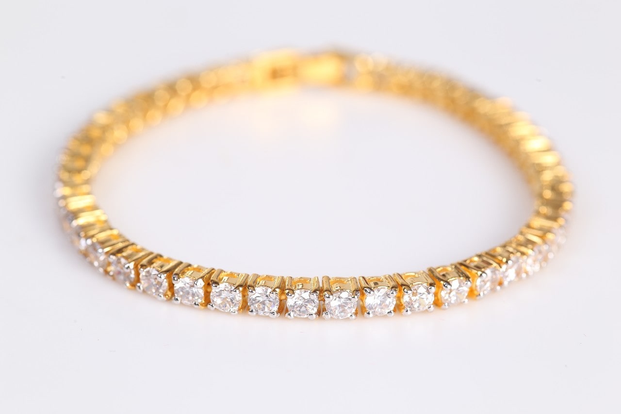 A yellow gold, diamond tennis bracelet on a white surface