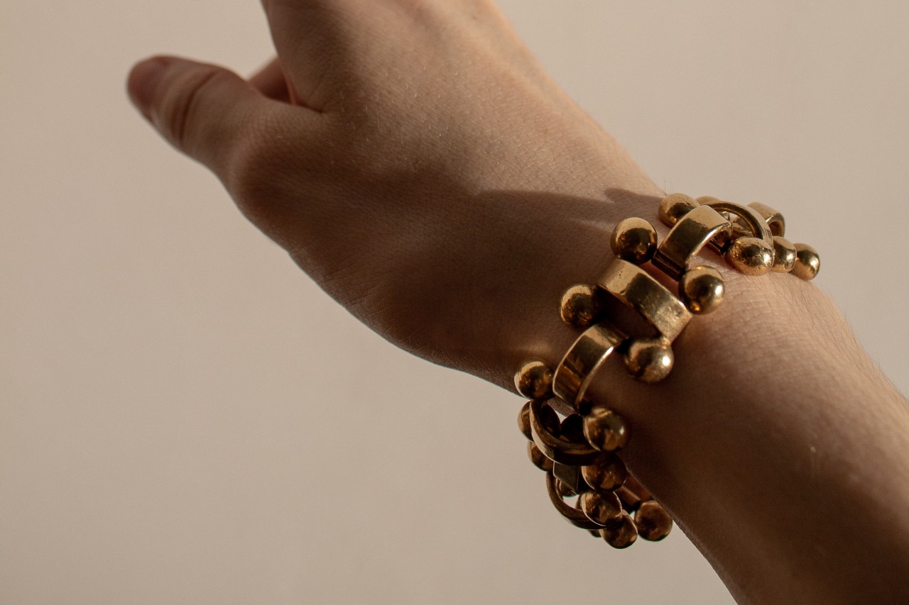 An extended arm reaching upwards, wearing a sculptural gold bracelet