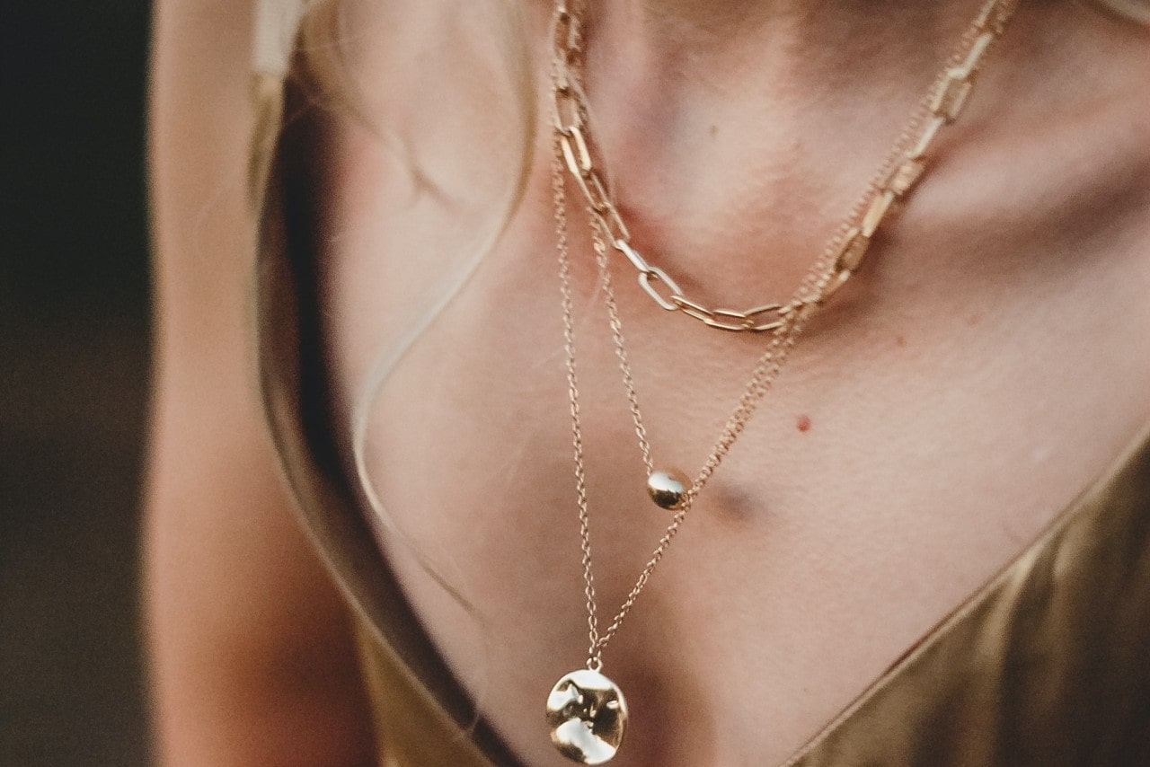 Close up image of a woman’s neckline, wearing three layered gold necklaces