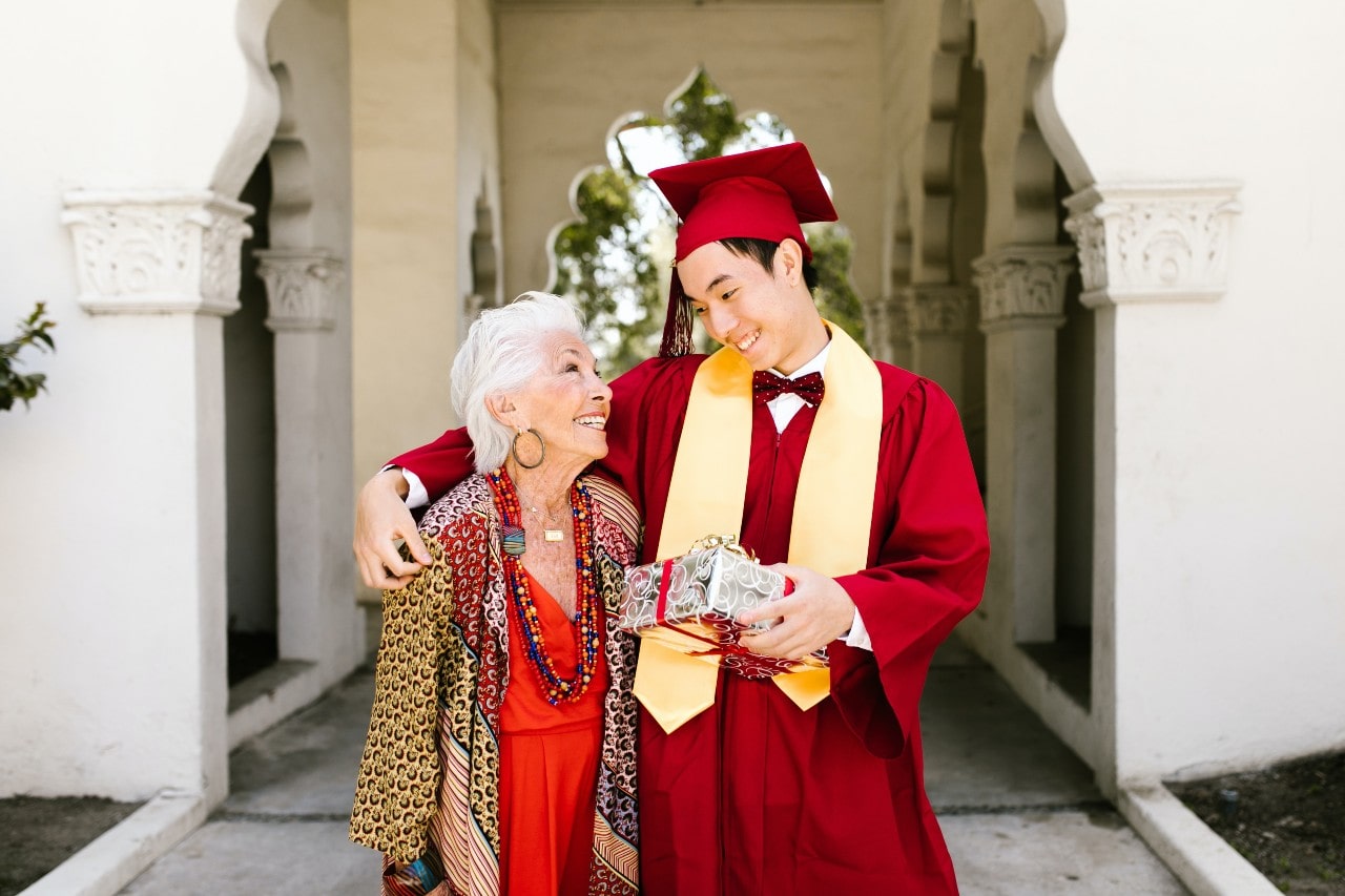 A graduate and his grandmother hugs while walking off of the campus