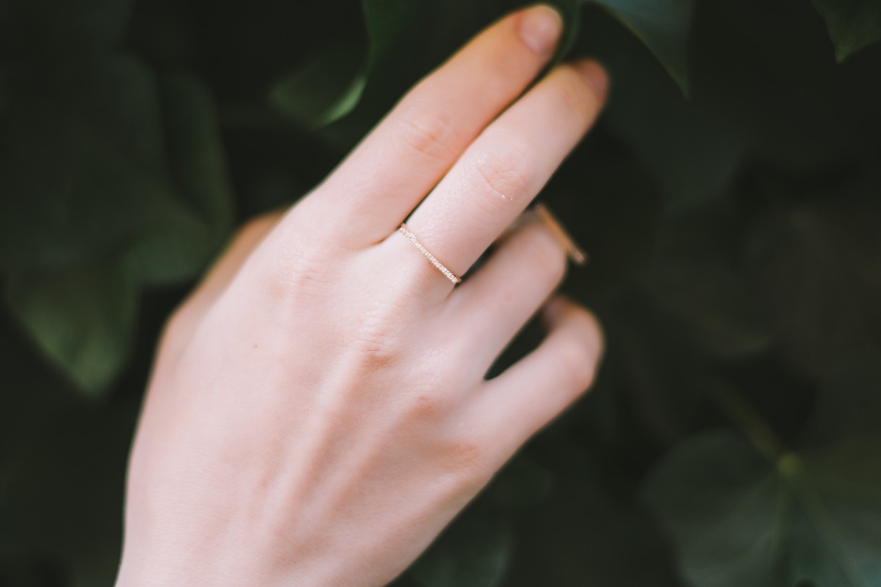 Close up image of a hand touching green leaves and wearing a simple gold and diamond ring