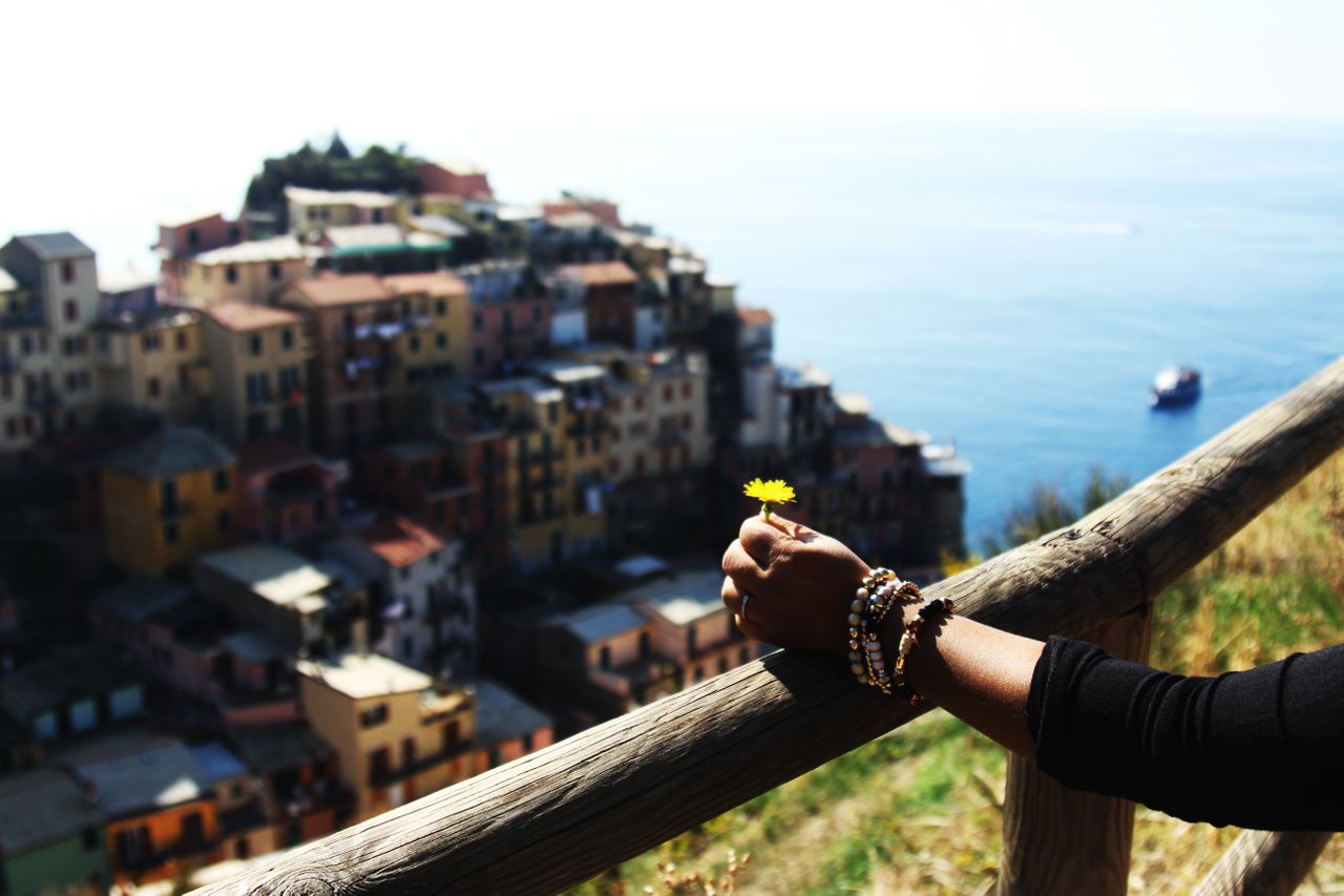 A woman holds a flower while walking up a hill overlooking a village.