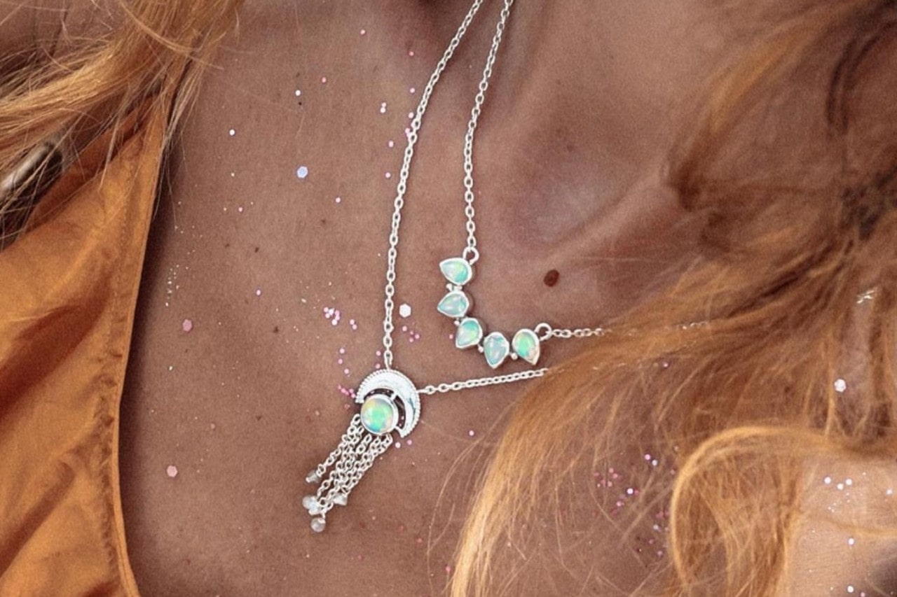 close-up image of a woman wearing two white gold and opal necklaces