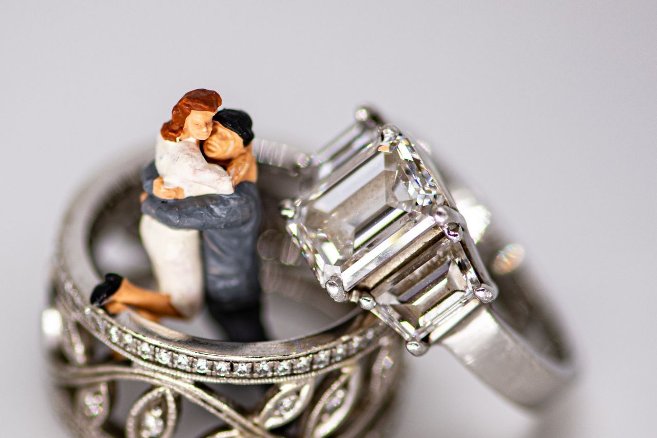 A three-stone platinum ring and a floral wedding band sit with a wedding cake topper.