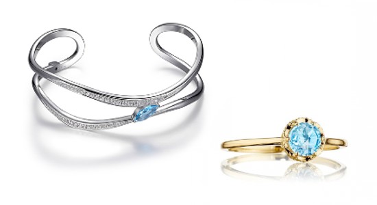 a white gold and blue topaz cuff bracelet next to a yellow gold and blue topaz ring