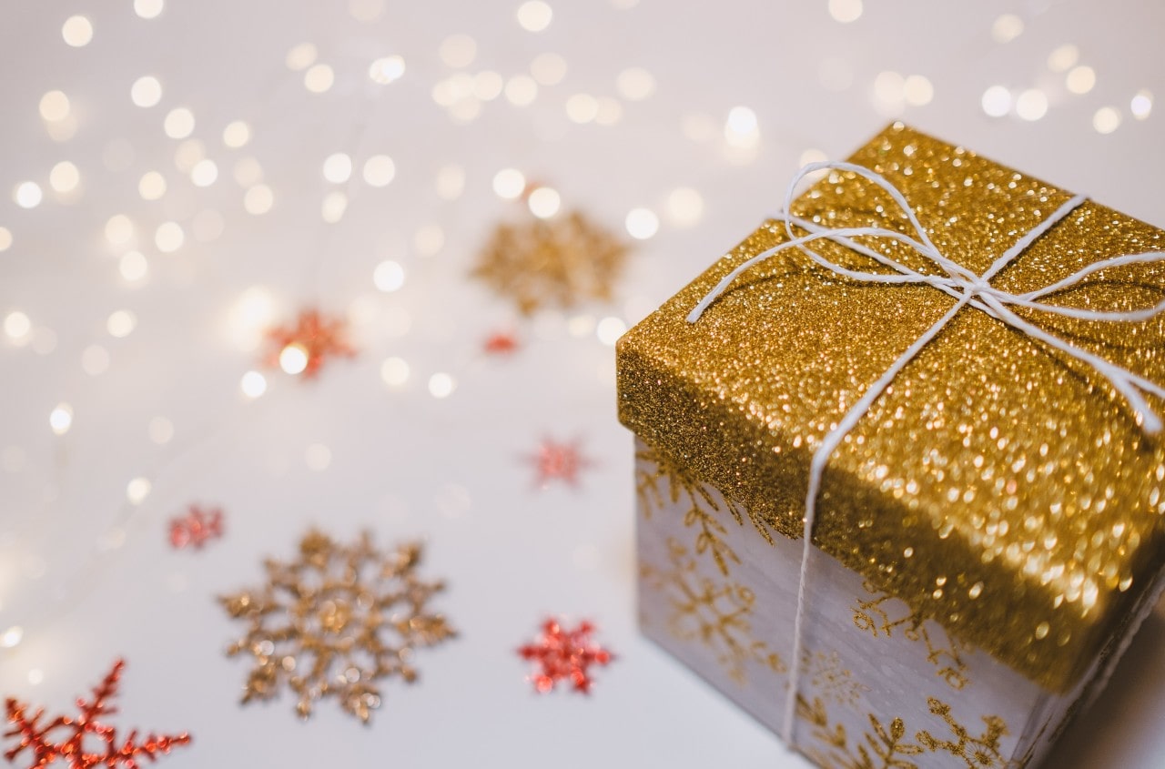 a wrapped gift sits by a white glittery snow scene with red snowflakes.
