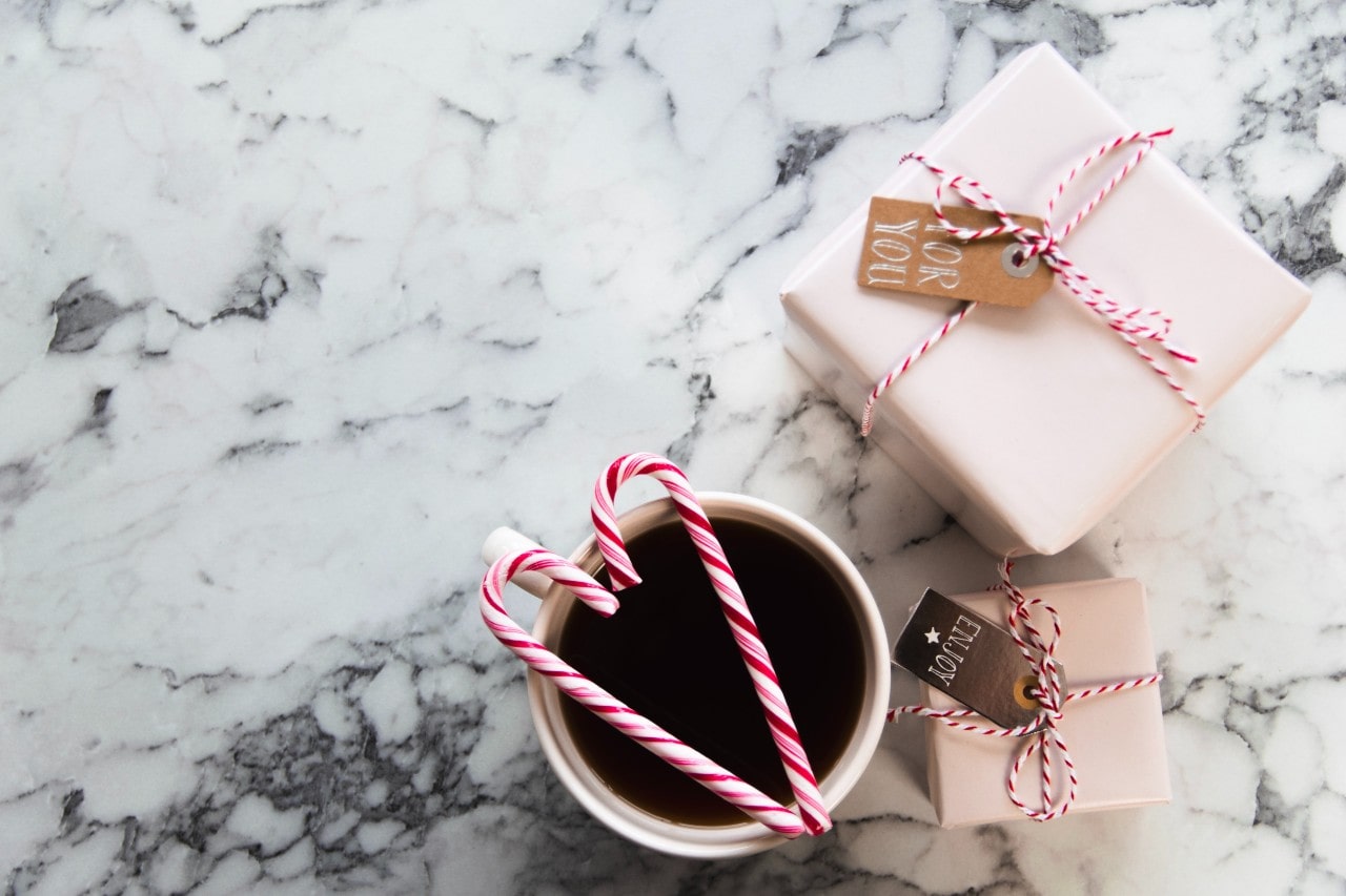 Two wrapped gifts sit by a coffee mug with two candy canes arranged in a heart on a kitchen counter.