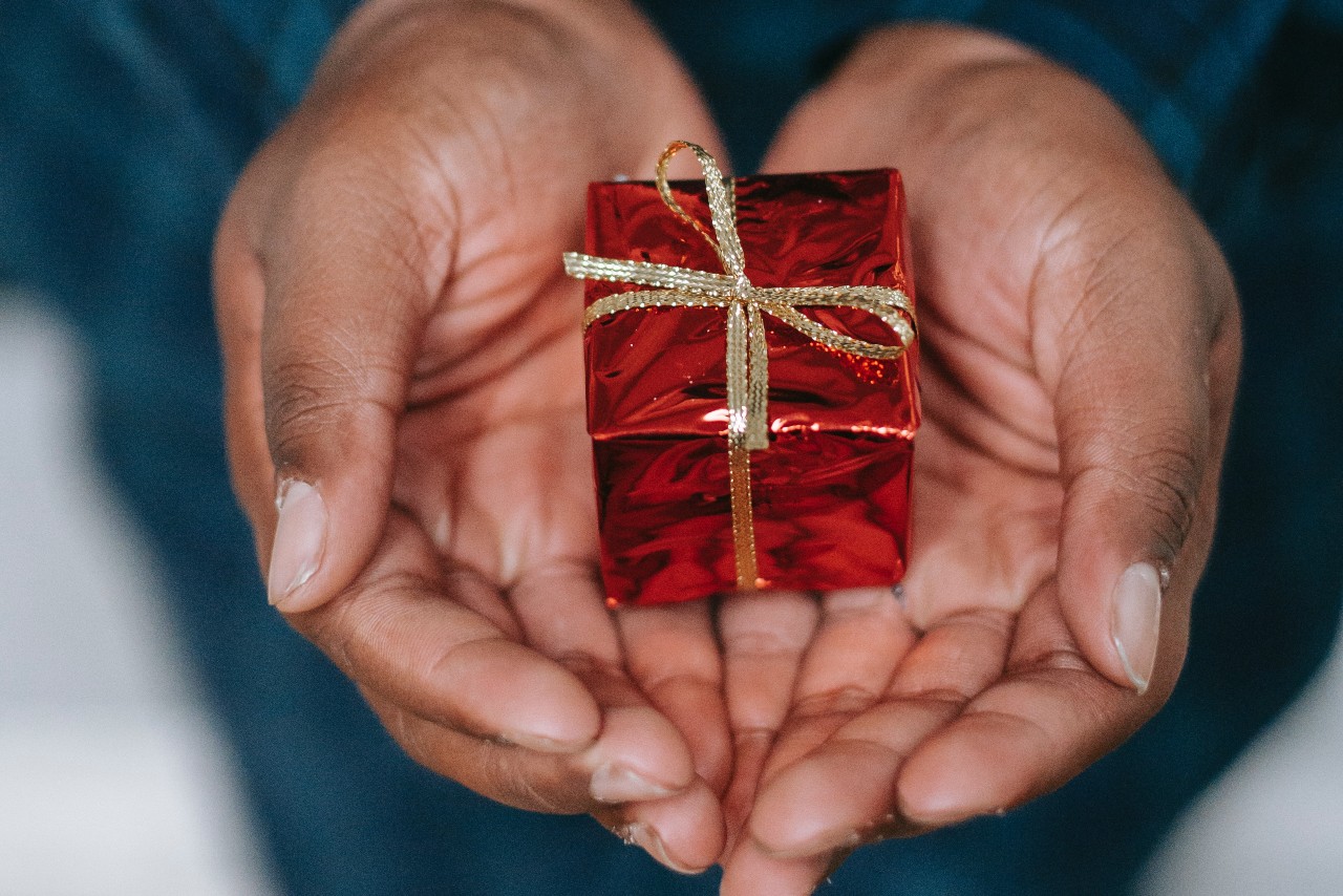 a small wrapped box sits in a person’s palm as it is offered to the recipient.