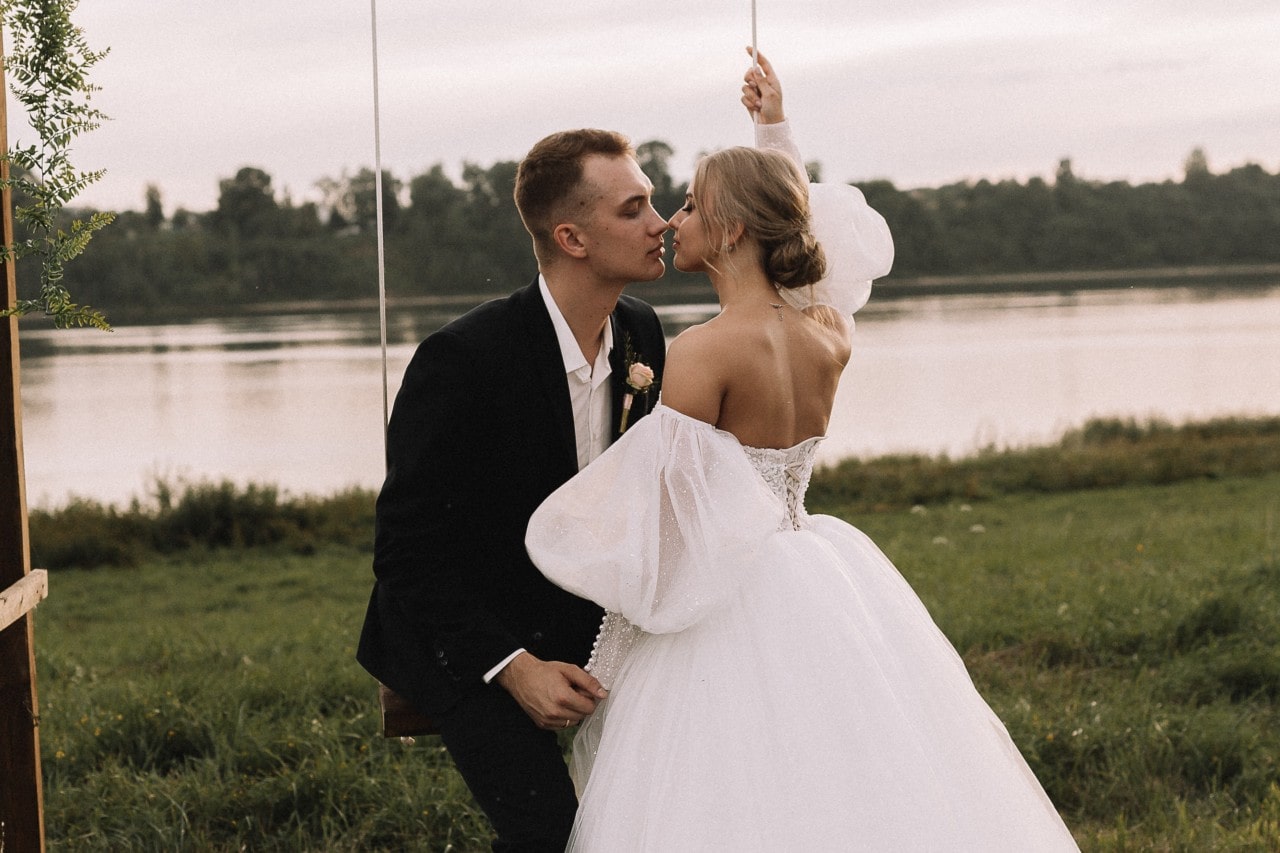 a bride and groom embracing on a swing by a lake