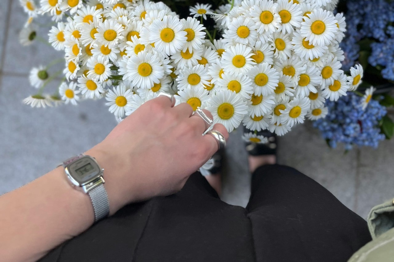 a person standing next to a bunch of daisies wearing a retro-inspired watch