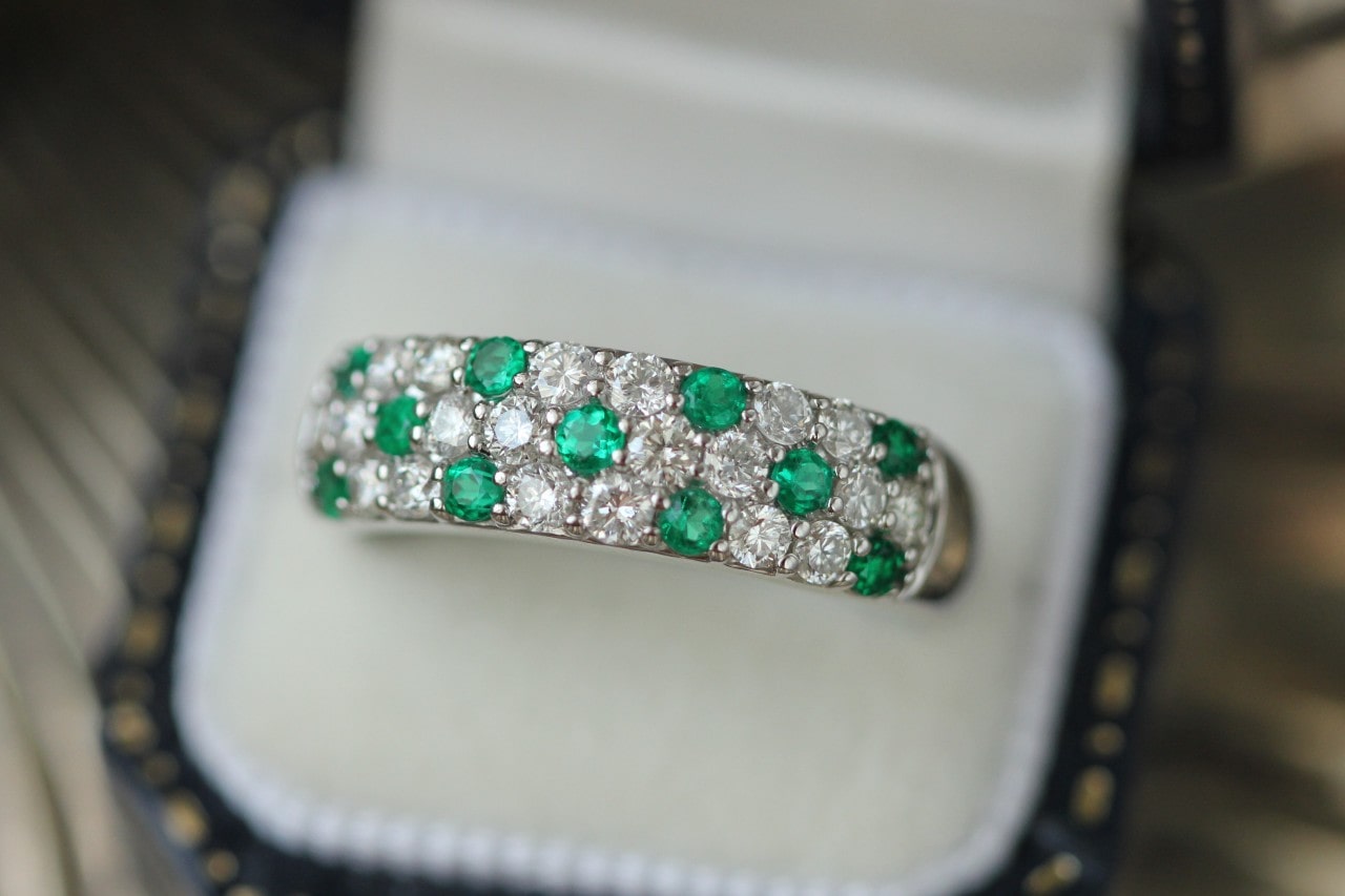 a silver wedding band featuring pave set, round cut diamonds and emeralds in a ring box