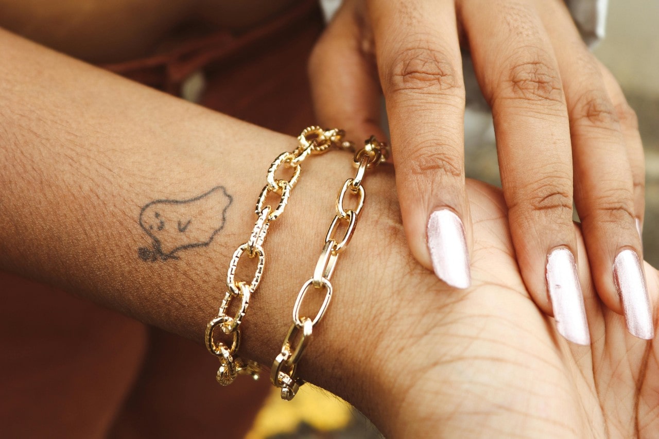 a woman’s wrist adorned with two gold chain bracelets