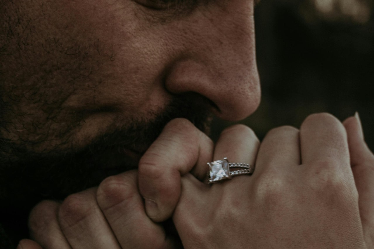 a man kissing his bride’s hand wearing an engagement ring