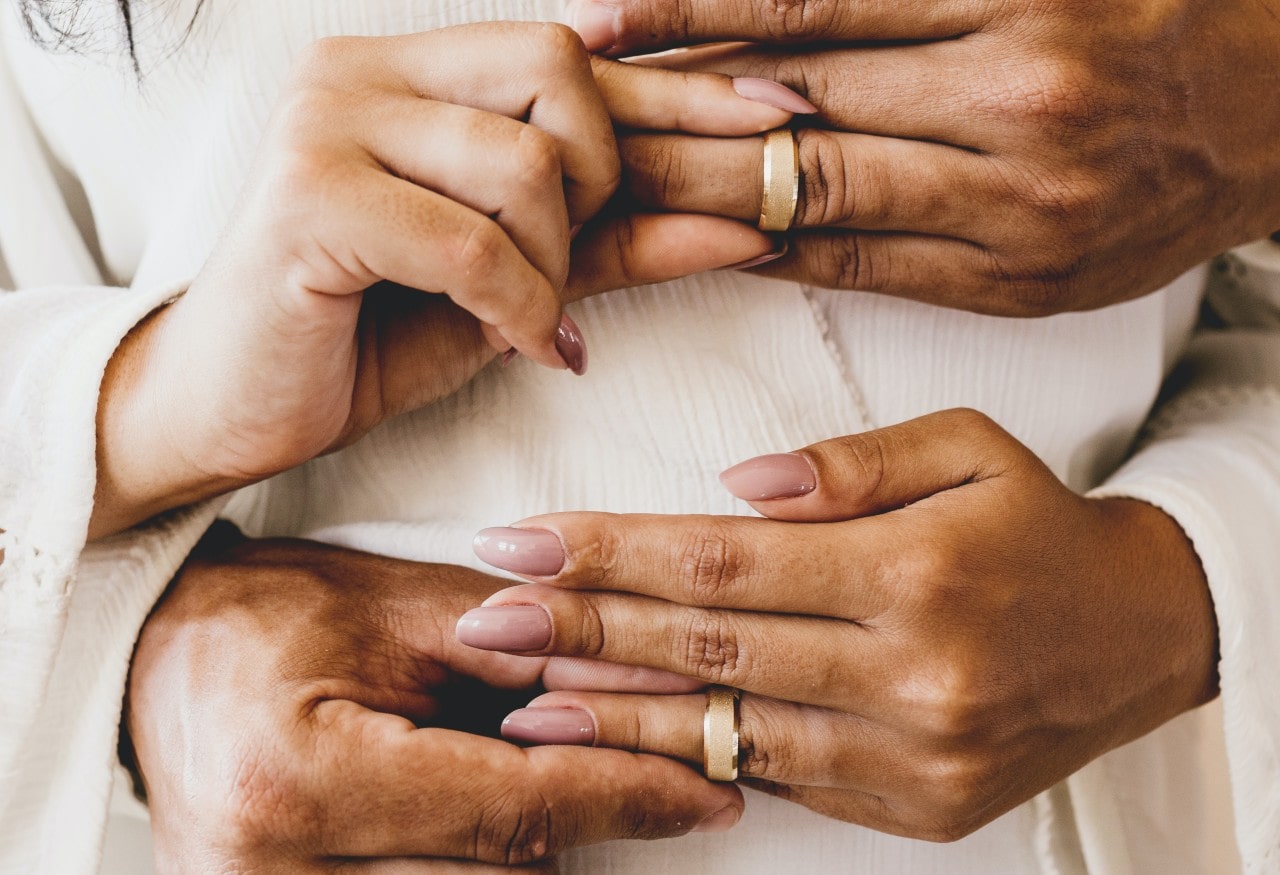 a couple simultaneously slipping matching wedding bands on each others’ fingers