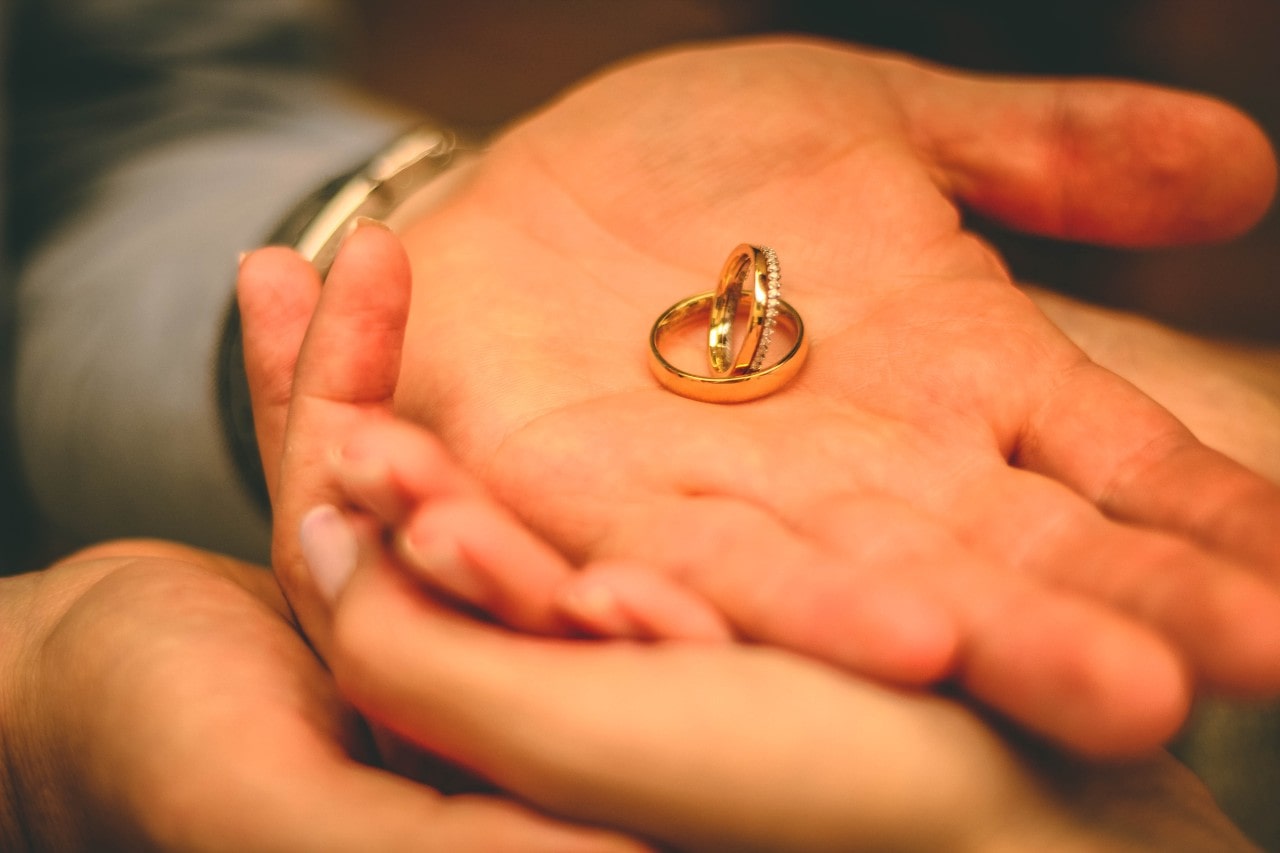 a couple’s hands holding a pair of yellow gold wedding bands