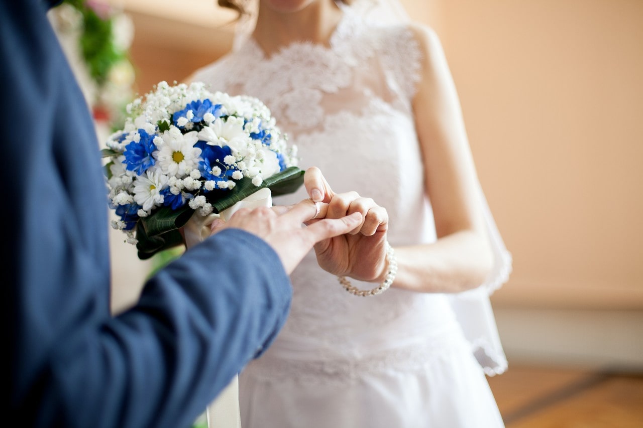 a bride slipping a ring onto her partner’s finger at the altar
