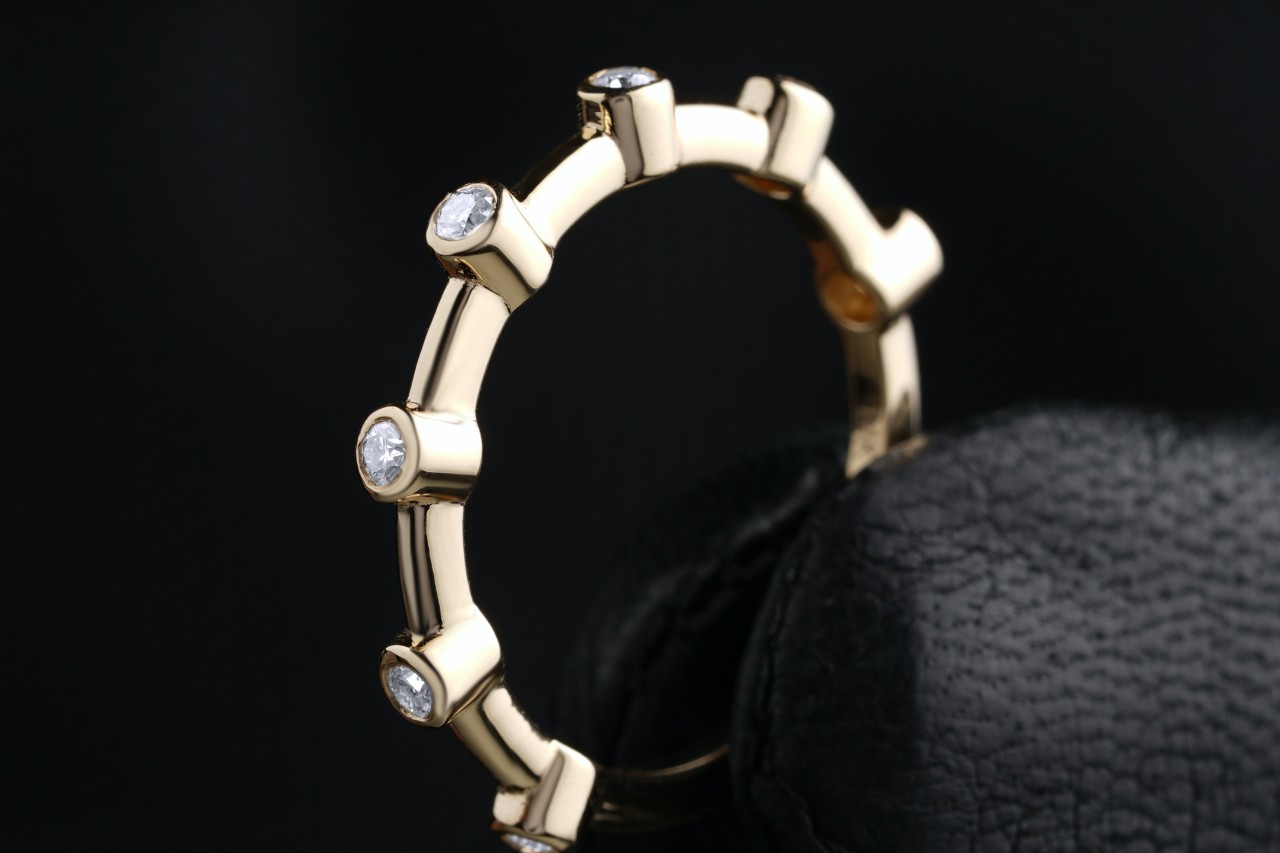 a yellow gold wedding band with bezel set diamonds against a black background