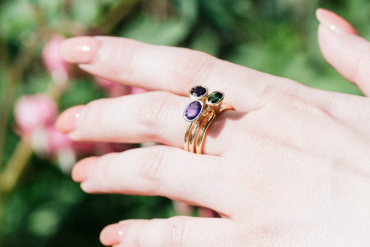 a woman’s hand wearing three stacked gemstone rings on the middle finger