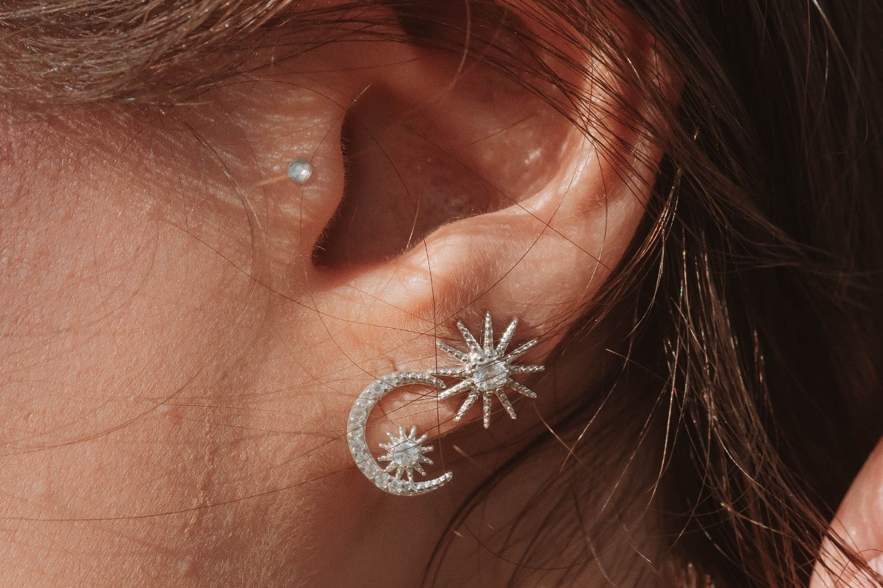 A close-up of a woman’s ear, adorned in sparkling sun and moon-inspired earrings.